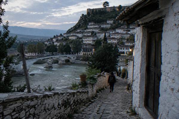 A cobbled lane climbing through Berat's old castle quarter between whitewashed stone walls and small wooden doors