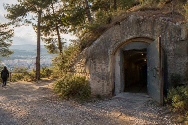 A heavy steel bunker door in a concrete wall set into a hillside, partly open on a dim corridor, Bunk'Art 1