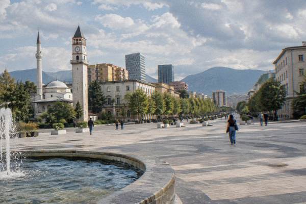 Pastel painted apartment blocks and a broad tree-lined boulevard in the centre of Tirana with a tram-free road and a few walkers, Skanderbeg Square