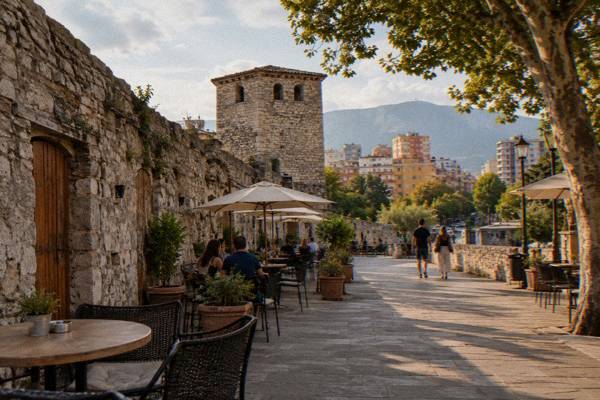 A restored old fortress wall with cafe tables along a pedestrian lane and wooden doors, Tirana Castle