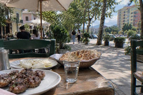 A small table at a Balkan cafe with plates of grilled meatballs, flatbread, white cheese and a glass of clear spirit, Blloku