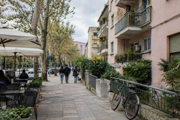 A pastel apartment block with a concrete balcony row beside a leafy street, a lone bicycle leaning on a railing, Blloku