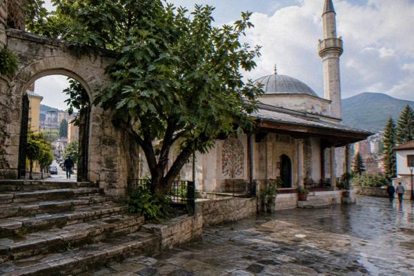 Worn stone steps and an arched gate in the older quarter beside a mosque courtyard with a fig tree, Et'hem Bey Mosque