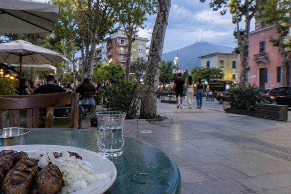 A plate of small grilled qofte meatballs with chopped onion and a tiny glass of raki on a street cafe table, Blloku