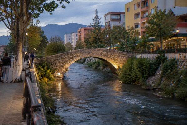 An old arched stone Ottoman bridge crossing a narrow stream among modern buildings in warm light, Tanners' Bridge