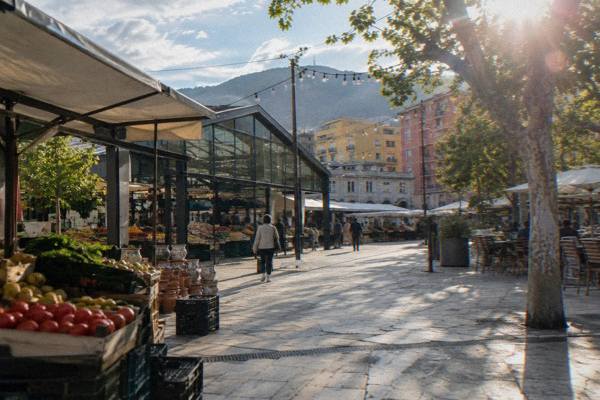 A renovated market square with glass-roofed stalls, ceramic pots and fruit crates and a pedestrian passing under string lights, New Bazaar
