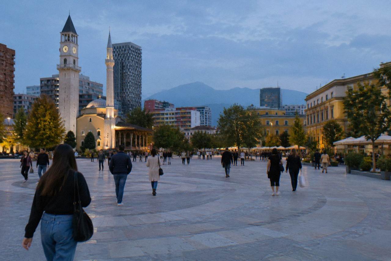Shoppers walking past cafés and shop fronts on a sunny street in central Tirana