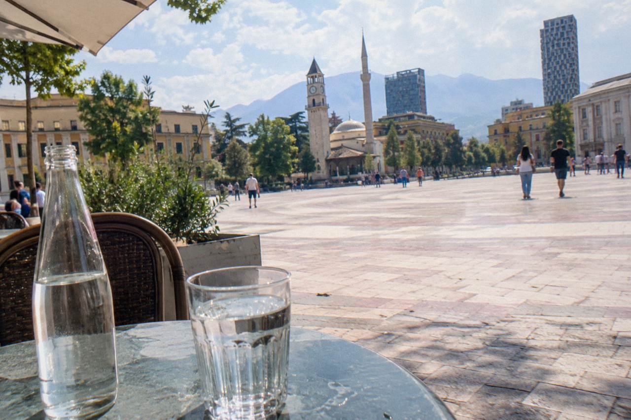 A glass water bottle and a full glass of water on a cafe table on a sunny Tirana street