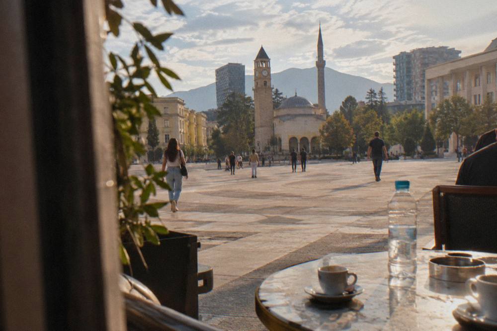 Espresso cups and a sealed water bottle on a marble cafe table in a busy Tirana square