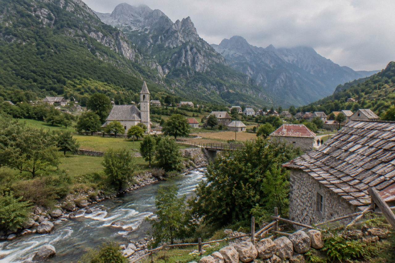 Stone houses of Theth village in a green valley beneath the peaks of the Albanian Alps