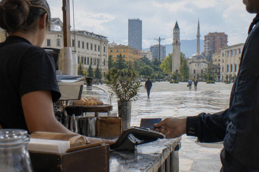 A customer paying with a bank card at a cafe counter in Tirana