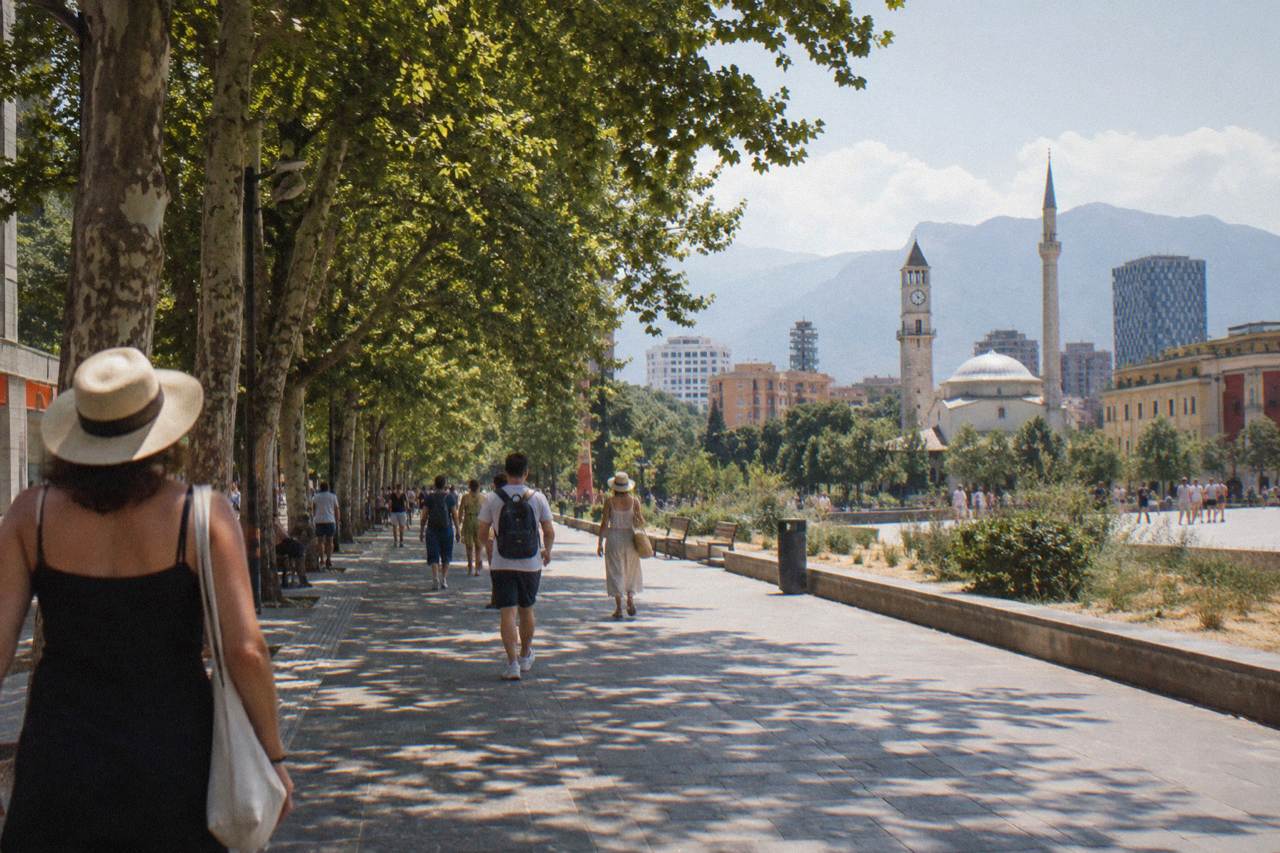 People in summer clothes walking along a tree-lined street in central Tirana