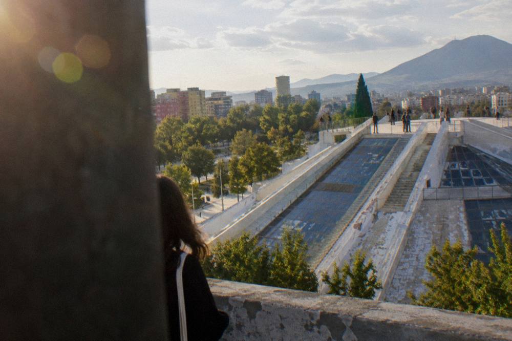The flat upper platform of the Pyramid of Tirana with people looking out over the city skyline