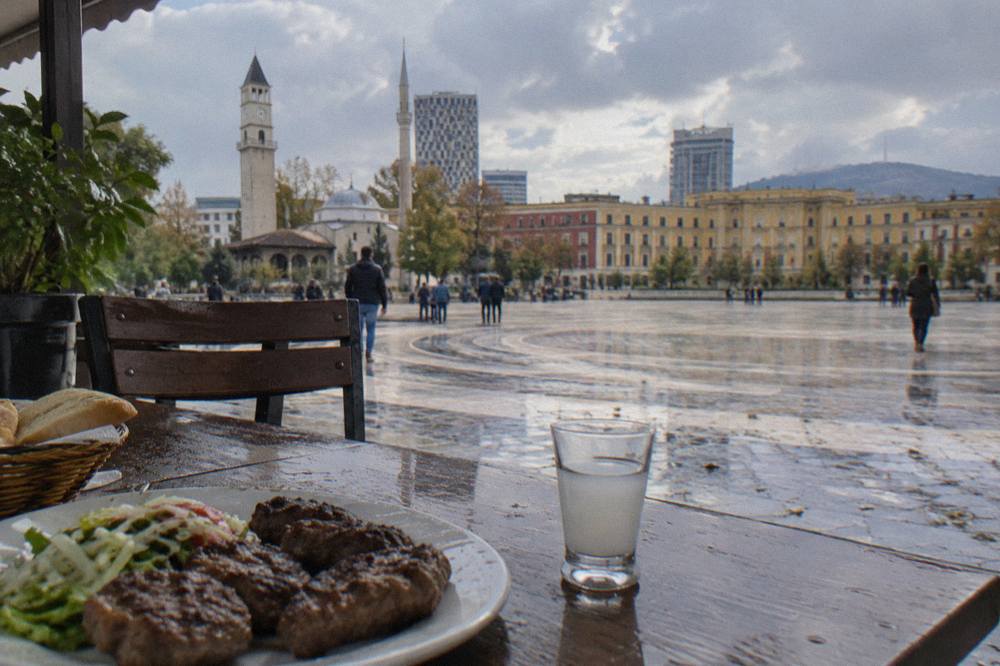 A small glass of raki beside a plate of qofte on a restaurant table in Tirana