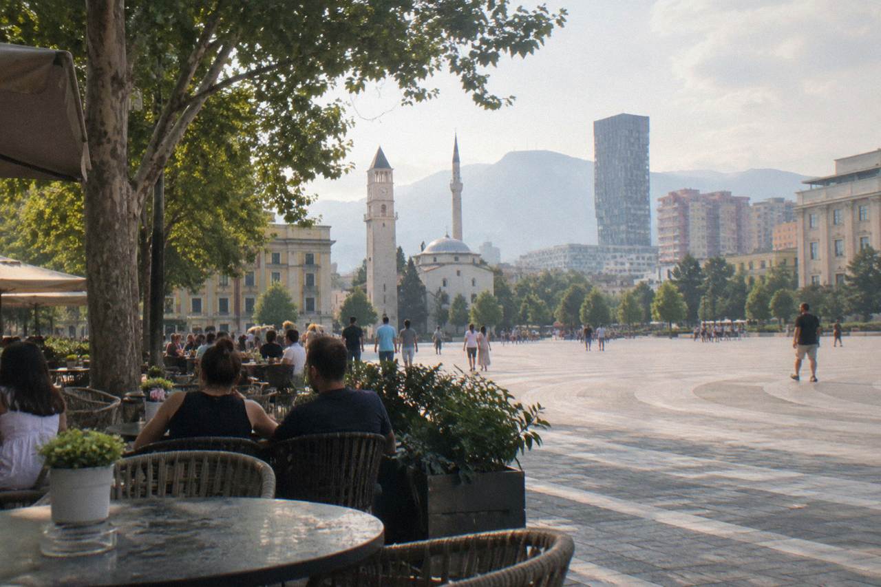 Cafe tables along a tree-lined street in central Tirana with people talking in the evening