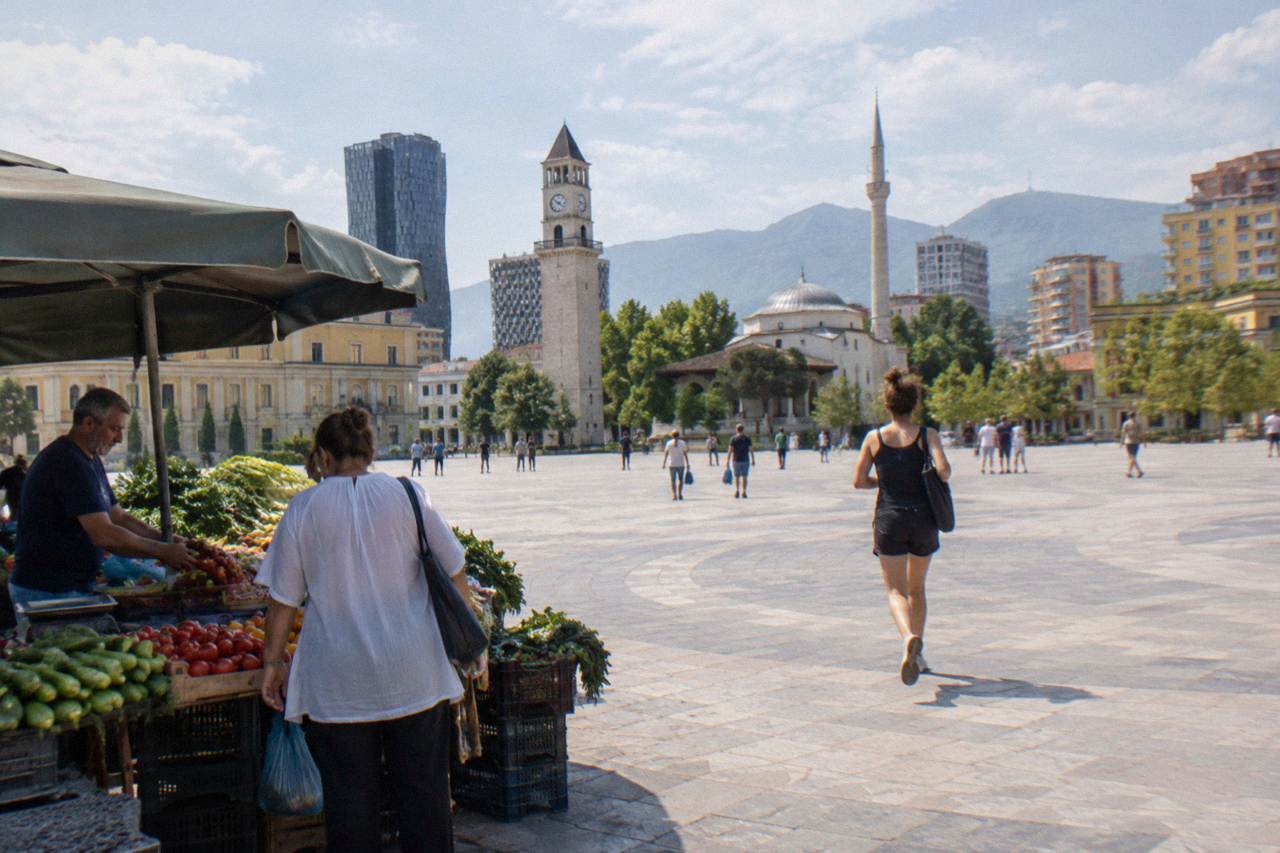 A market stall in central Tirana with fresh produce and a vendor serving a customer