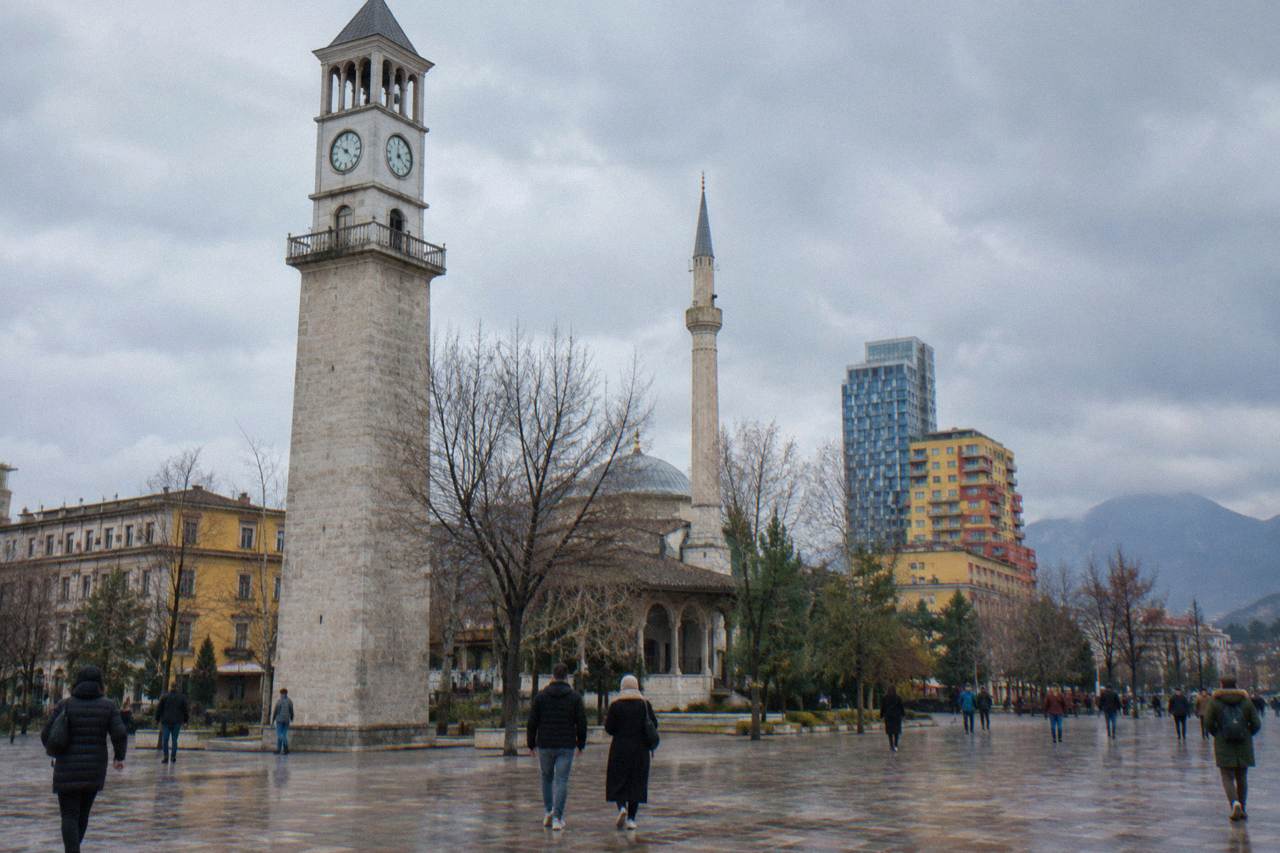 Skanderbeg Square in Tirana under an overcast winter sky, with the Clock Tower and mosque minaret behind bare trees