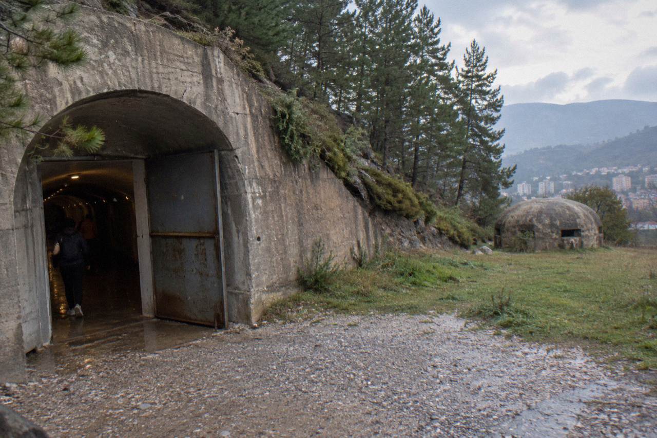 A small concrete dome bunker standing in a grassy field with hills behind it