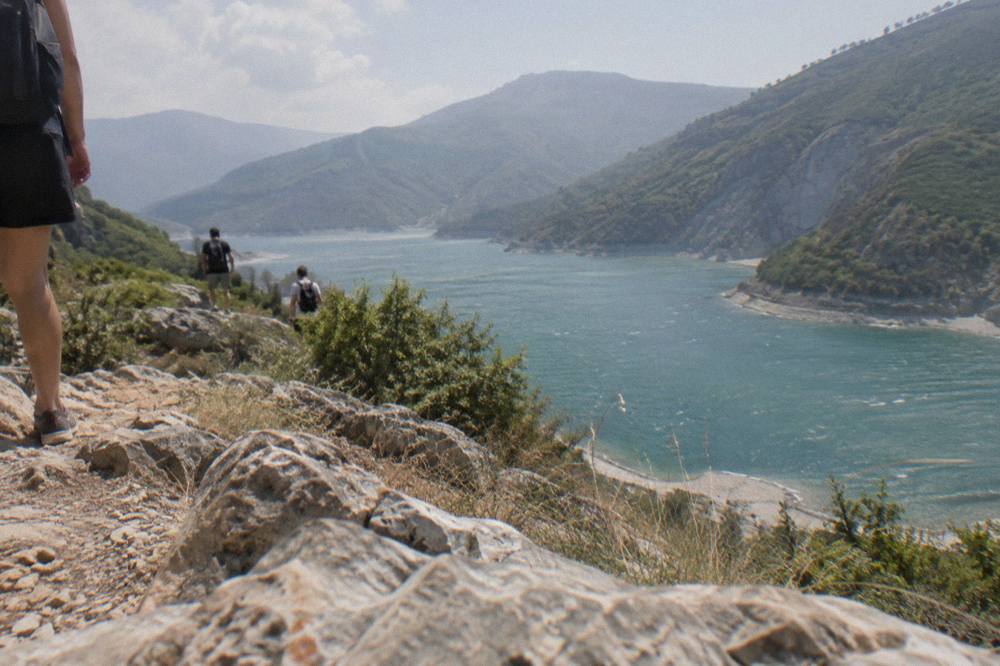 Hikers on a rocky mountain ridge looking down at a blue reservoir between steep hills