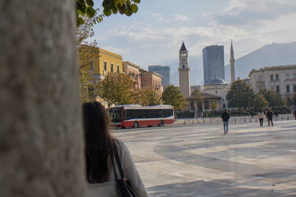 A red-and-white city bus passing colourful buildings on a boulevard in Tirana