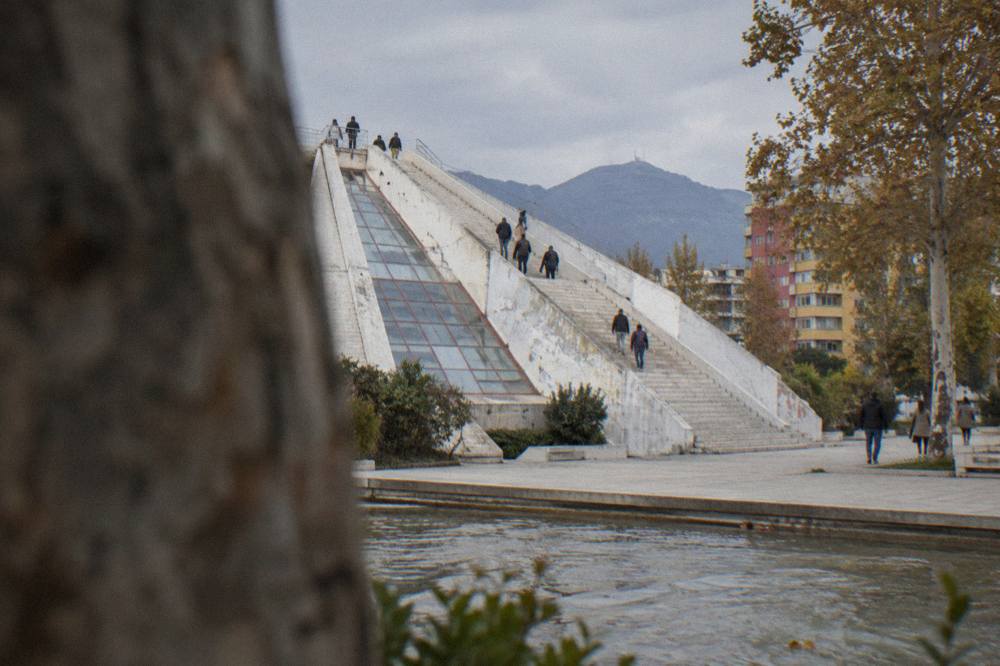 The stepped exterior of the renovated Pyramid of Tirana with people climbing the sloped steps to the viewing platform
