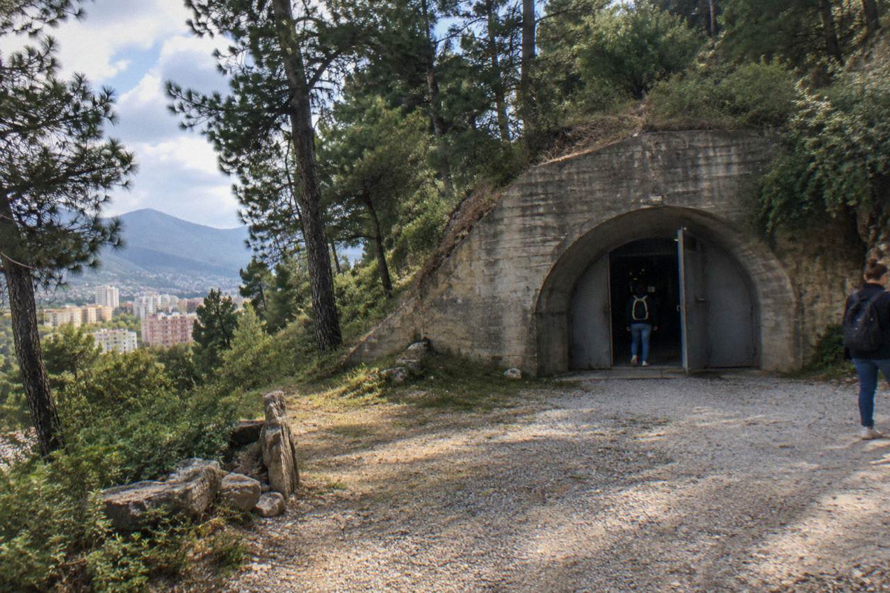 A heavy concrete bunker entrance set into a hillside on the edge of Tirana