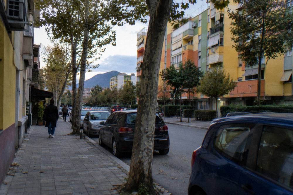 A residential street in Komuna e Parisit with apartment blocks and plane trees