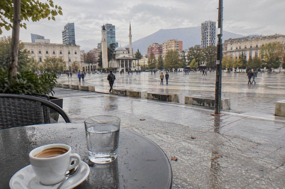 An espresso coffee and a glass of water on a small cafe table on a Tirana sidewalk