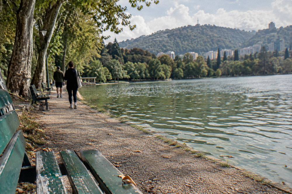 Walkers on a gravel path beside the Artificial Lake in Tirana with wooded hills behind