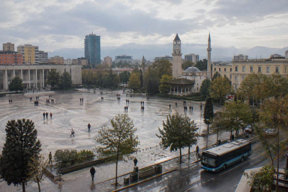 A city bus on a Tirana street with apartment buildings and trees behind it