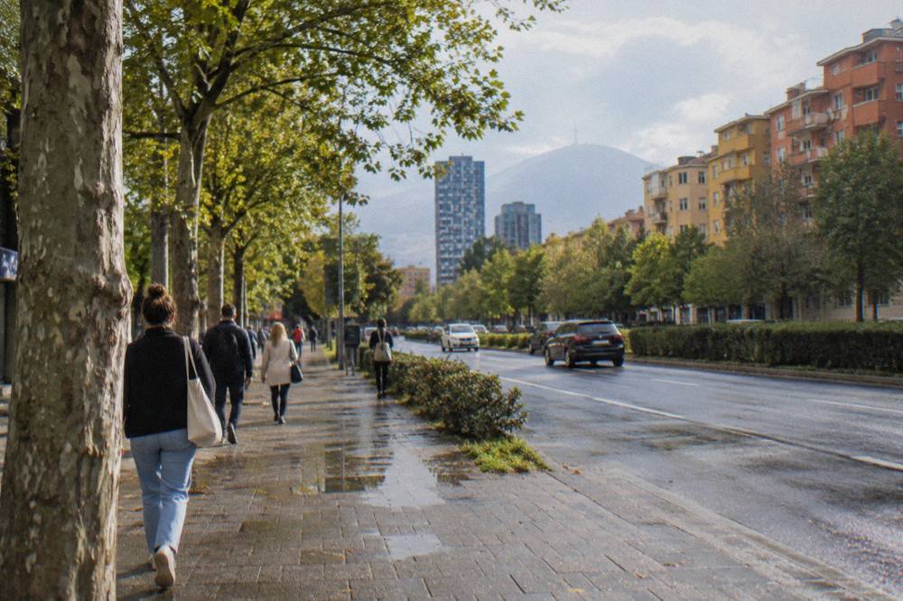 Pedestrians crossing a tree-lined boulevard in a residential district of Tirana