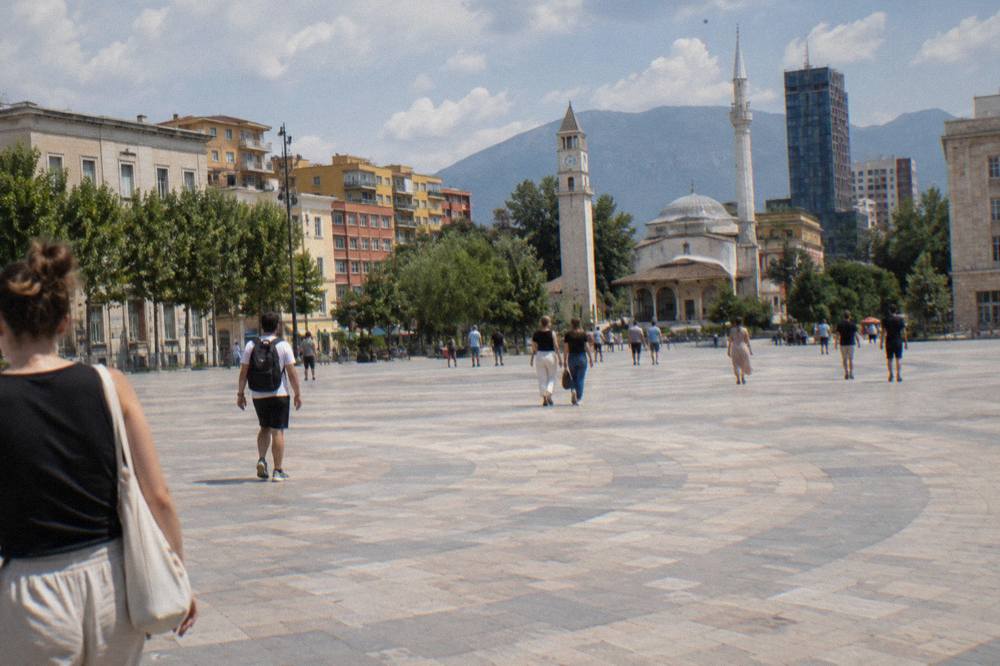 People walking across the stone surface of Skanderbeg Square on a sunny afternoon