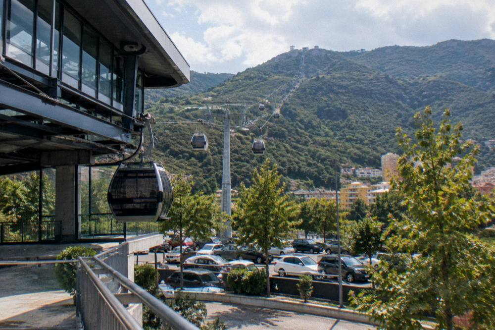 Cable car cabins rising through green hills toward Mount Dajti above Tirana