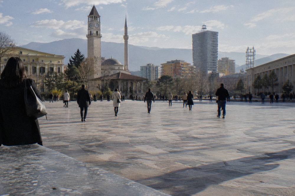 People crossing a broad pedestrian square in central Tirana on a sunny afternoon