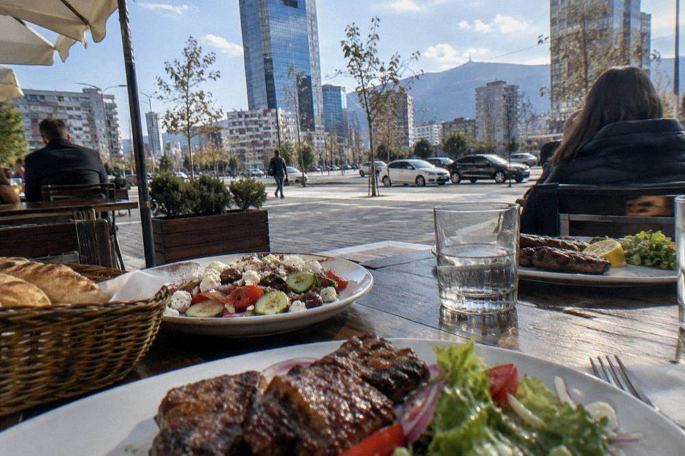 Diners at an outdoor market restaurant with grilled meat and salad plates