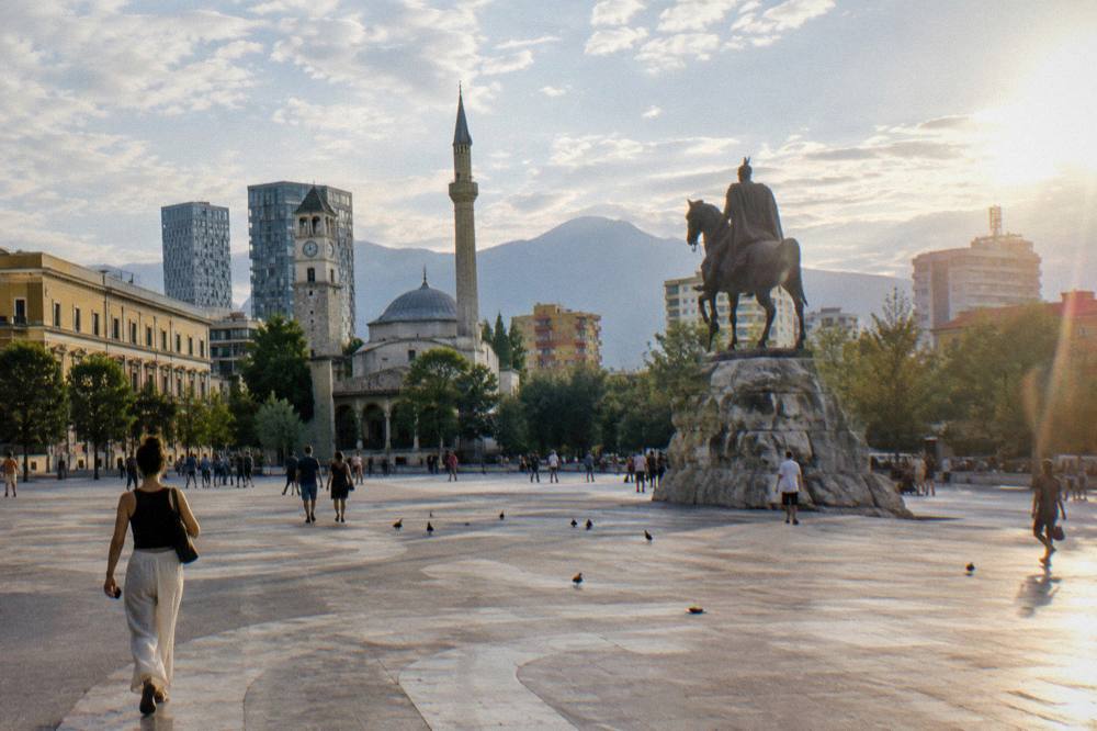 Wide pedestrian square in Tirana with an equestrian statue and mosque minaret