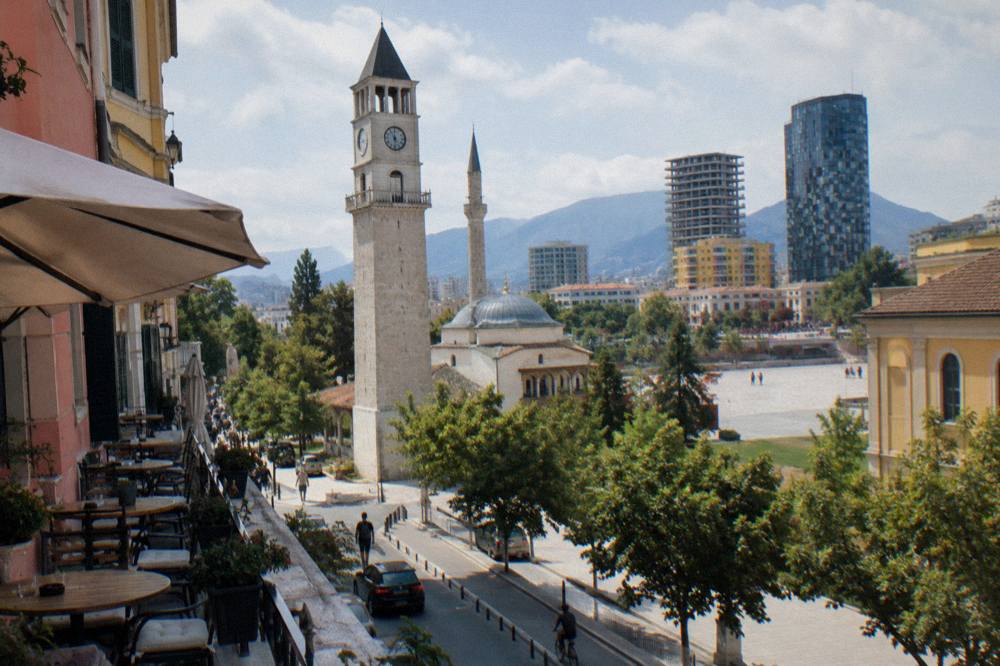 The Clock Tower seen from a side street with cafe tables and pastel facades in the foreground