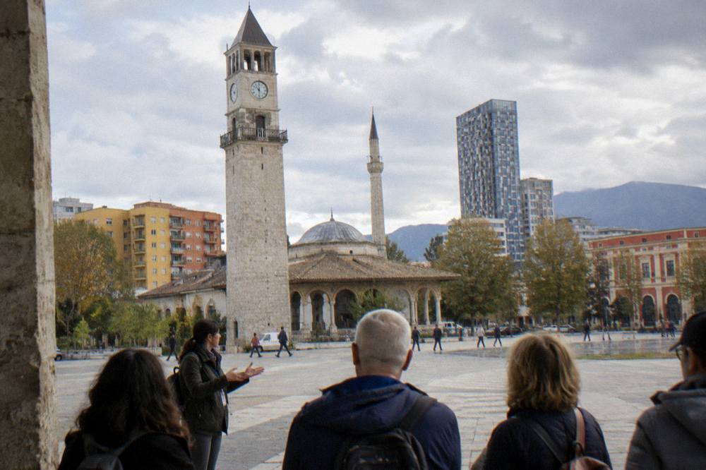 A guide speaking to a small group of visitors beside the Clock Tower on Skanderbeg Square