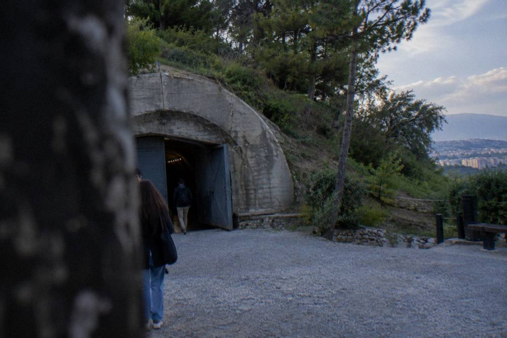 The concrete entrance of a bunker museum beside a green hillside at the edge of Tirana