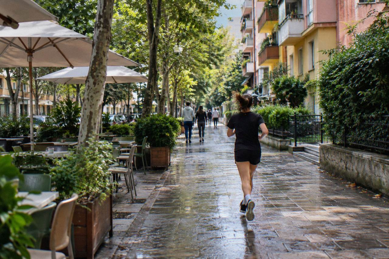 A leafy residential street in Blloku with apartment blocks and cafes under trees