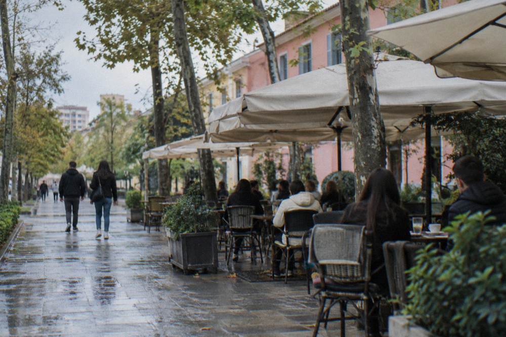 People sitting at outdoor cafe tables on a shaded Blloku street