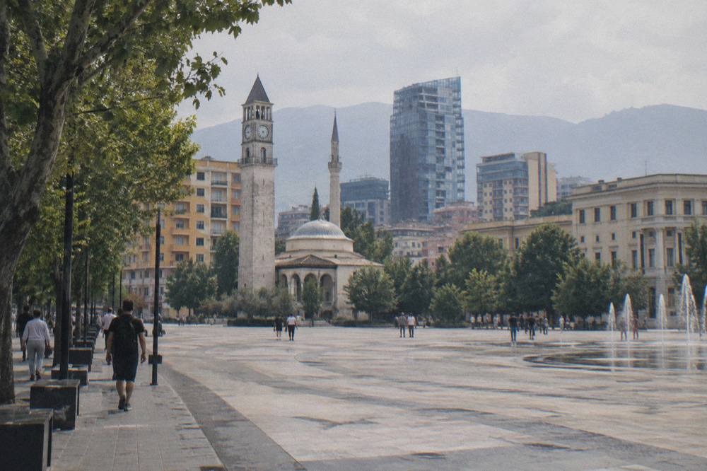 A city boulevard in Tirana with trees and buildings under an overcast sky