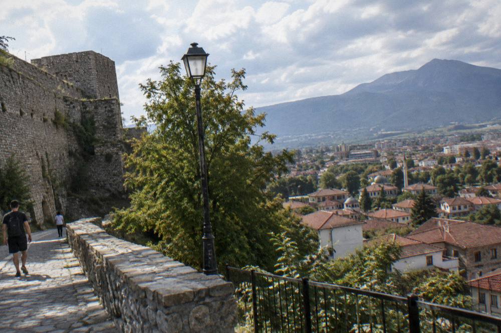 A stone castle wall above a town of tiled roofs on a hillside