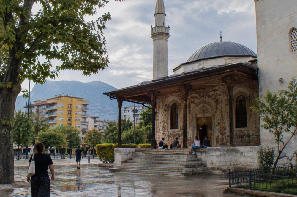 Tourists resting on the stone steps in front of the painted entrance porch of the Et'hem Bey Mosque