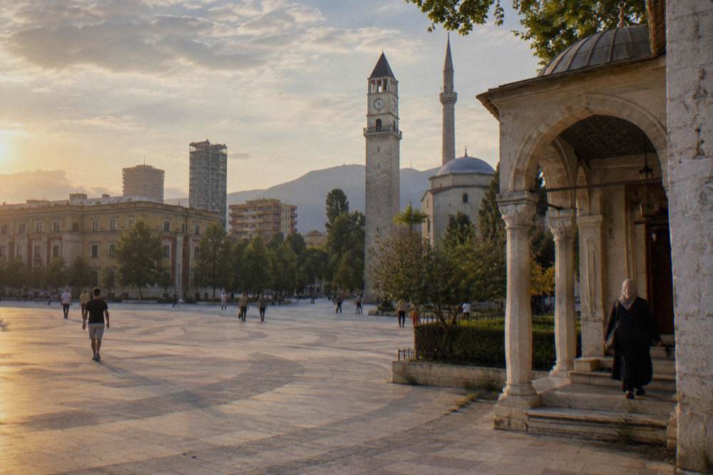A woman in a headscarf and covered shoulders entering the mosque porch in Tirana