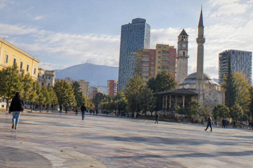 The small minaret of the old mosque rising beside taller modern buildings in central Tirana