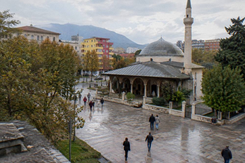 People crossing the wide pedestrian square toward the mosque on a bright afternoon
