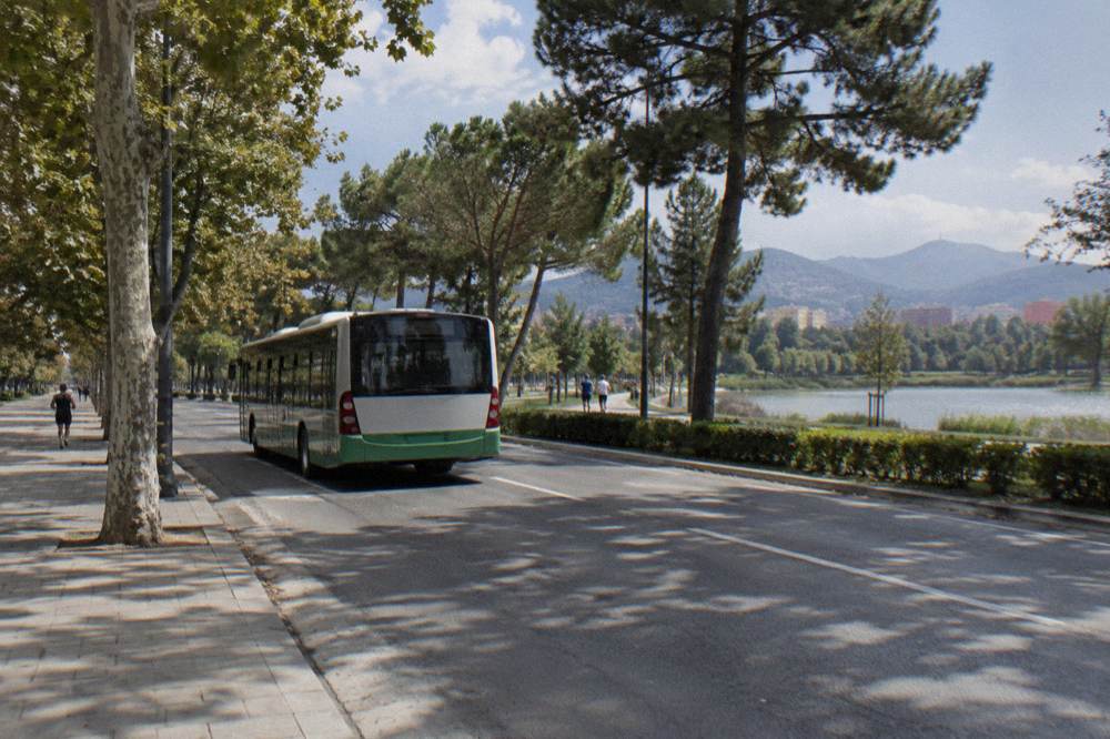 A city bus passing along a tree-lined boulevard toward the Grand Park of Tirana
