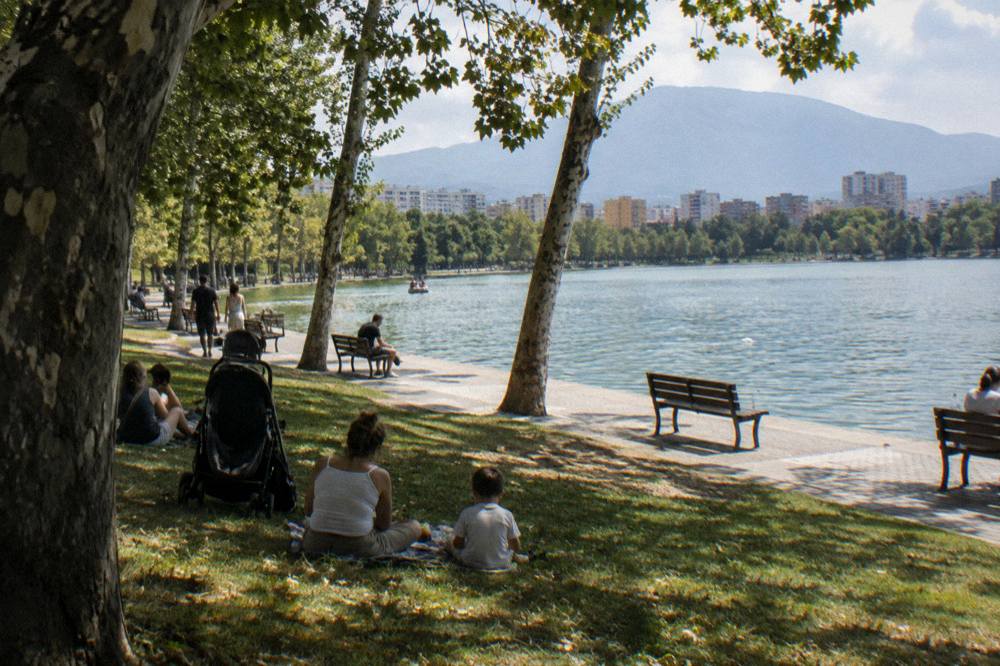 Families and strollers on a lawn beside the Artificial Lake in Tirana on a warm afternoon
