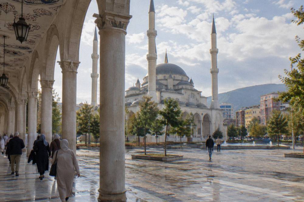 Visitors in modest clothing walking through the mosque's columned arcade